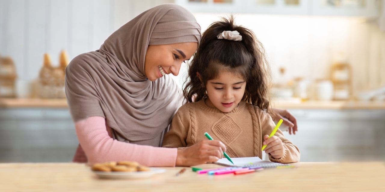 a woman wearing hijab assisting a little girl on her paper works