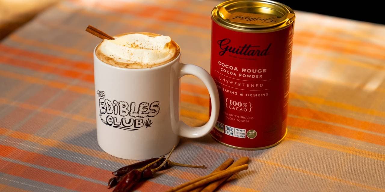 A cup of hot chocolate with a cinnamon stick and a Calabrian chili