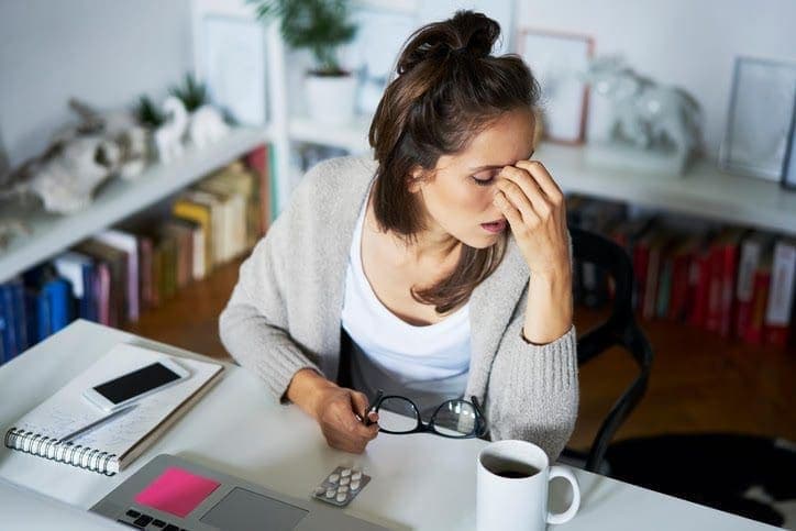 woman holding her nose and the other hand her eyeglasses down the table